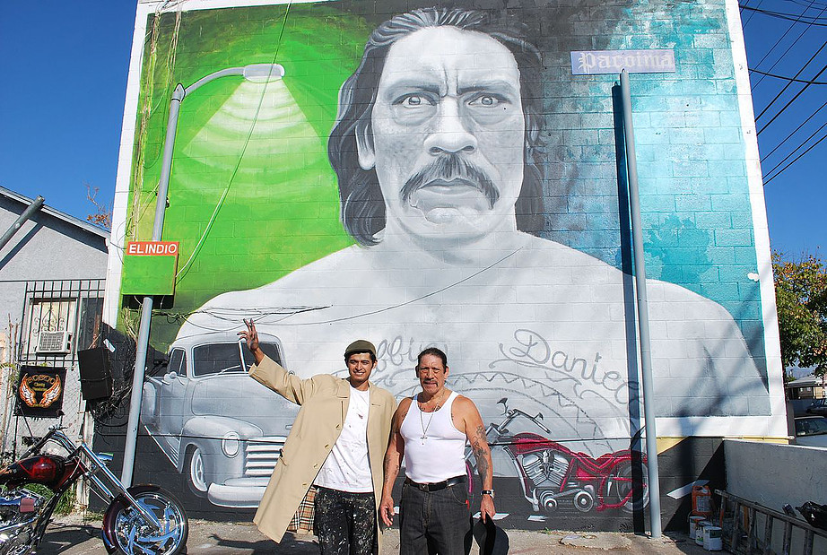 Photograph of muralist Levi Ponce and actor Danny Trejo in front of a mural of the actor by the muralist in Pacoima. The project is part of the Celebrate Pacoima initiative.