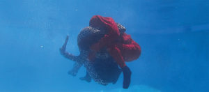 A still from a video of DCA Cultural Trailblazer Suné Woods' work. Two people, one dressed in red the other in leopard print tussle under water.