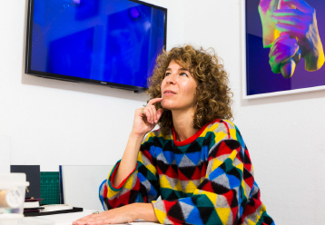 Cultural Trailblazers 2020-2021 - Julie Weitz looks up to the sky from the interior of her studio. In the background are paintings and a computer screen