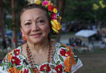 Promise Zone Arts. A woman wearing flowers in her hair and a traditional Mexican dress tenderly looks into the camera len